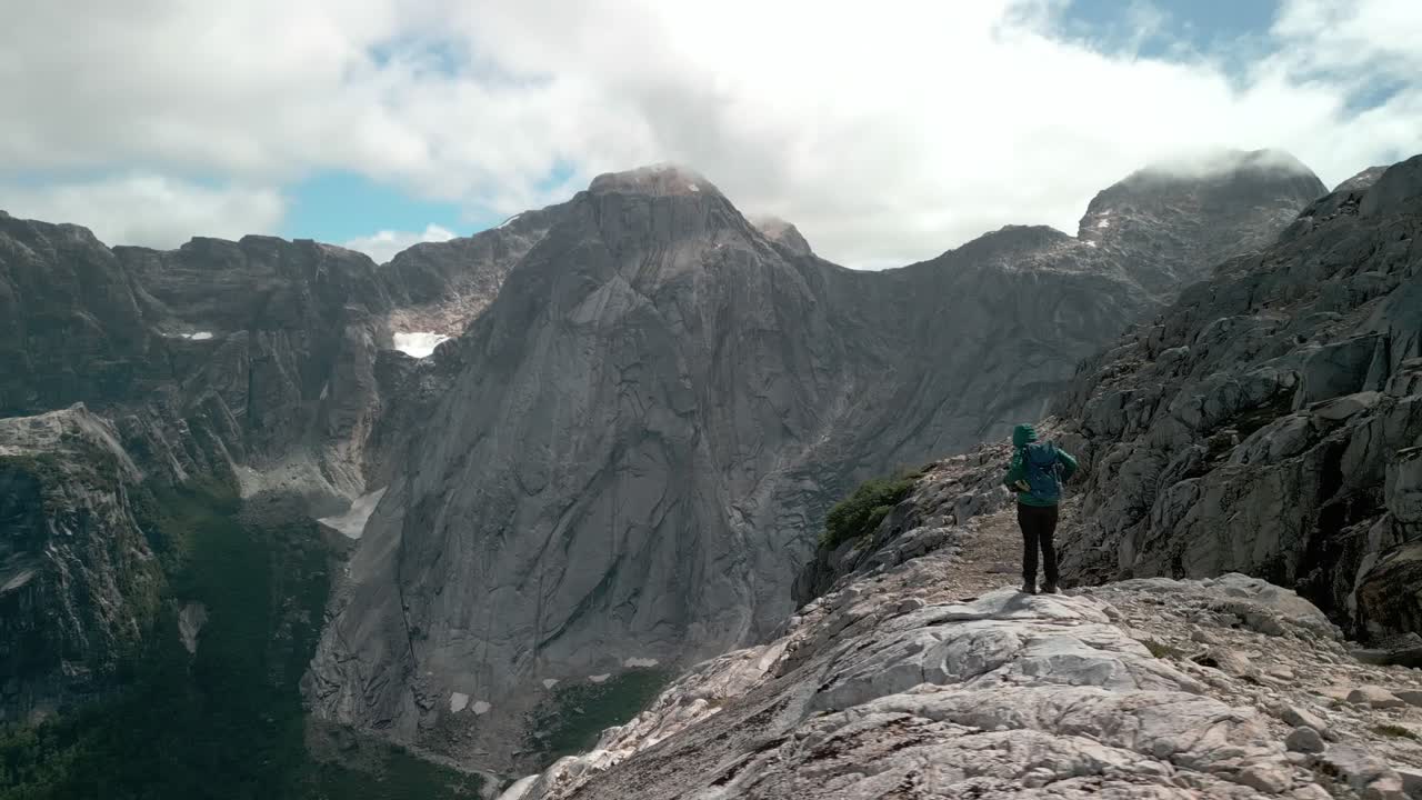 excursionista preparándose para un sendero mientras el dron lo rodea y le permite ver un valle remoto con una gran montaña al fondo