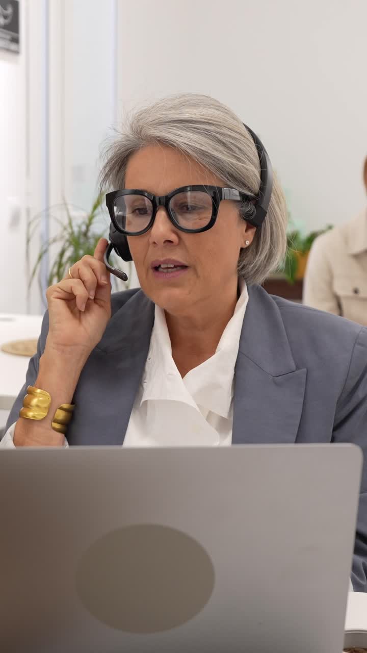 Donna matura con cuffie che lavora al laptop in ufficio