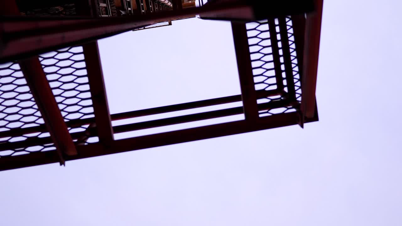A spinning rotating shot looking up at a red ladder fire escape attached to an old industrial historic building in the city downtown. In 4k slow motion.