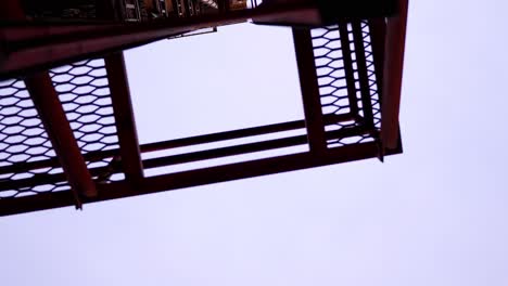 a spinning rotating shot looking up at a red ladder fire escape attached to an old industrial historic building in the city downtown. in 4k slow motion.