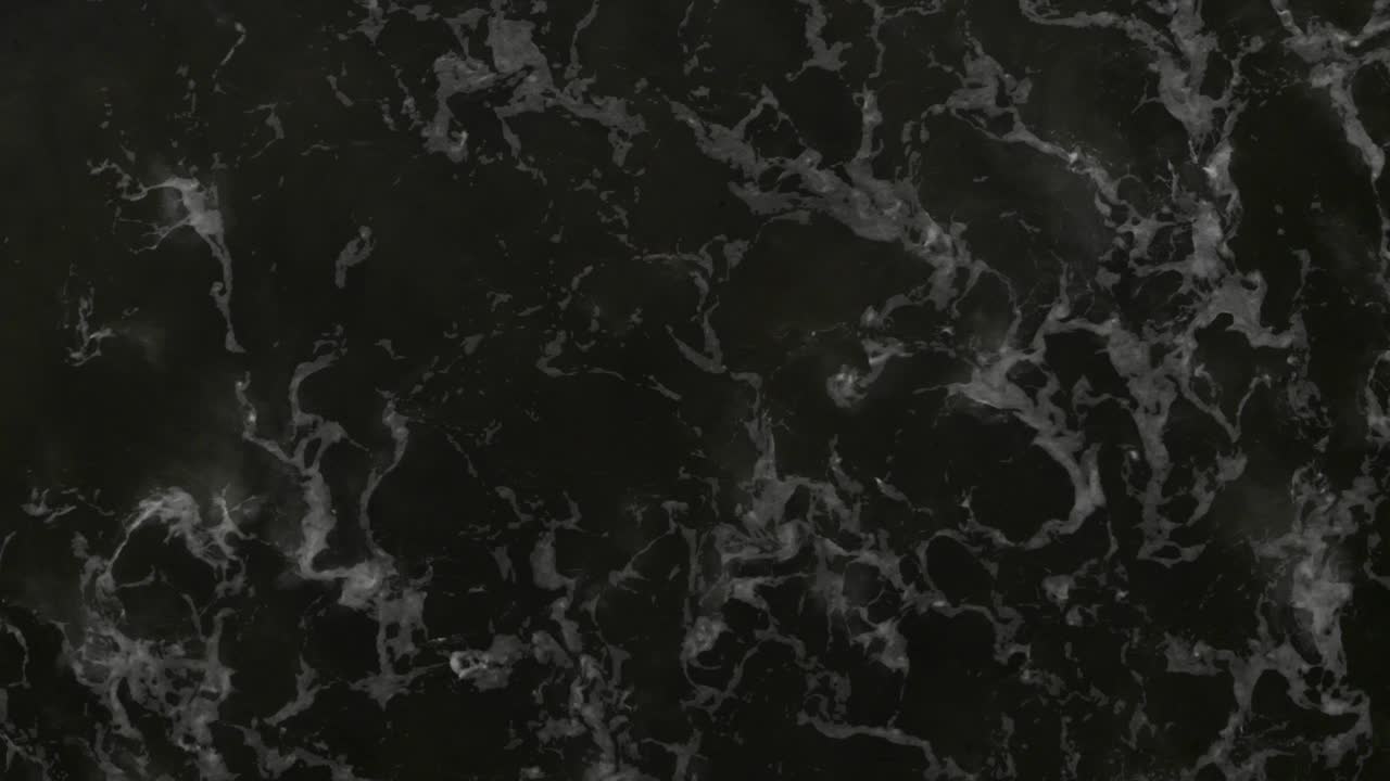 Drone shot of waves crashing diagonally over dark ocean with camera straight down