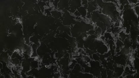 drone shot of waves crashing diagonally over dark ocean with camera straight down