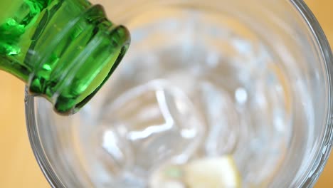 pouring sparkling water into a glass with ice and lemon