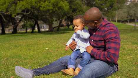 Father-raising-up-boy-from-grass,-making-him-seated-on-knees