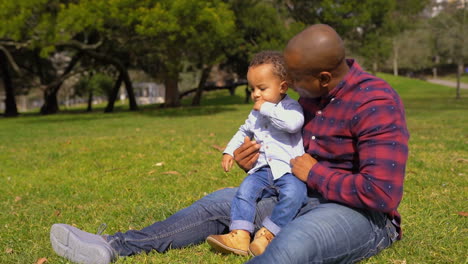 father raising up boy from grass, making him seated on knees