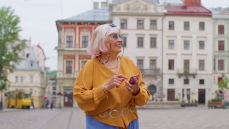 Elderly-stylish-tourist-woman-looking-for-way-find-route-using-smartphone-in-old-town-Lviv,-Ukraine