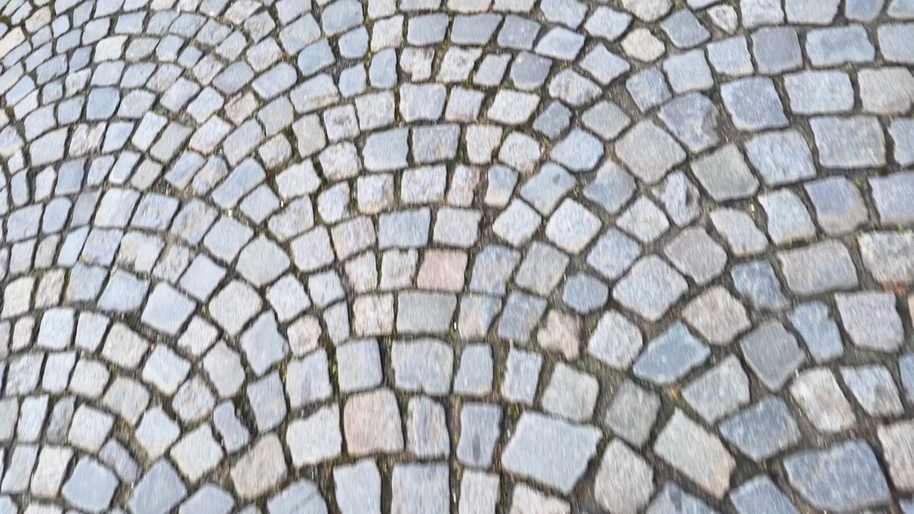 A handheld camera moves over ancient granite cobblestones arranged in a fan pattern outdoors