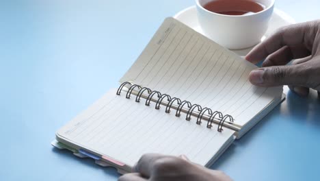 person writing in a notebook with a cup of tea