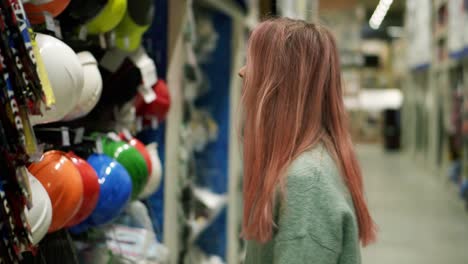 Young-Girl-Looking-For-Colorful-Protection-Helmet-In-Hardware-Store