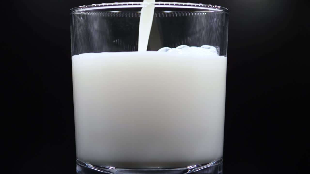 verter leche en un vaso transparente, aislado en fondo negro - cerrar