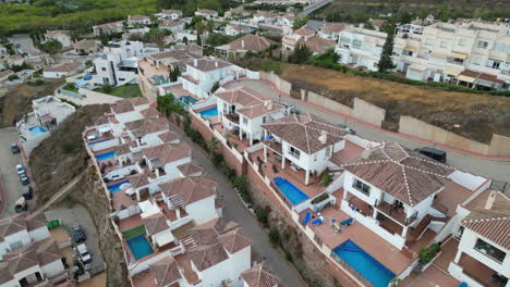 Camera-rising-up-from-expensive-holiday-homes,-pools-and-gardens-then-revealing-mountains-in-the-distance