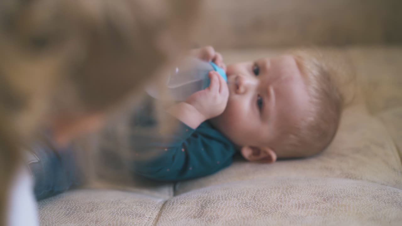 el bebé bebe agua de la botella y la hermana mayor en la cama