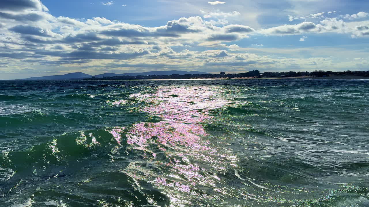 Onde si infrangono lungo la costa a mezzogiorno con nuvole e montagne visibili all'orizzonte sullo sfondo