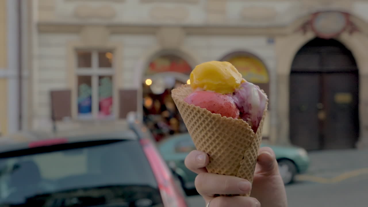Vista ravvicinata al rallentatore di una donna che cammina e mangia palline di gelato con uno sfondo di paesaggio urbano sfocato, Praga, Repubblica Ceca