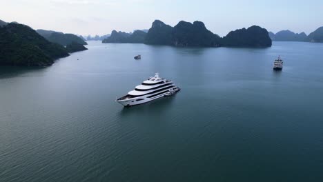 aerial of beautiful white luxury yacht anchored in ha long bay vietnam with large limestone cliffs at sunset