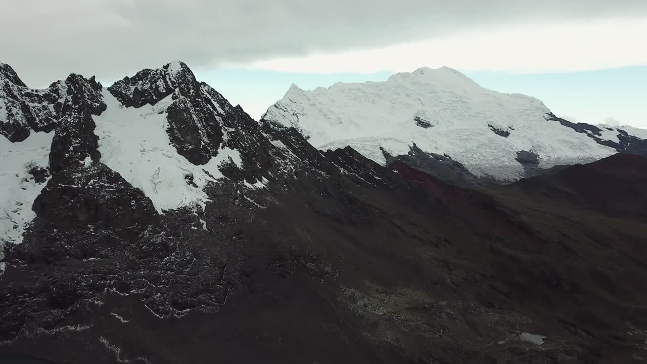 Aerial, drone shot overlooking rocky and snowy, Andean mountains, cloudy day, in Pitumarca, Peru, South America