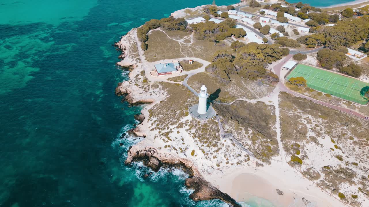 Cinematic aerial footage panning around the Bathurst Lighthouse on Rottnest Island. The lighthouse is surrounded by sandy white beaches and the turquoise blue ocean
