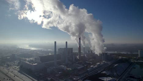 Toma-Aérea-En-órbita-Amplia-De-Una-Central-Eléctrica-De-Calefacción-Alimentada-Por-Carbón-Con-Un-Espeso-Humo-Blanco-Proveniente-De-Las-Chimeneas-Que-Genera-Smog-Gris-Sobre-El-Horizonte.