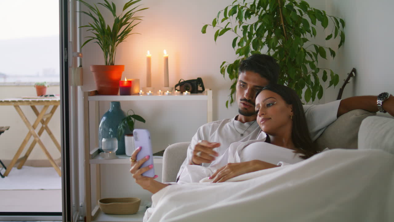 pareja casada viendo el teléfono inteligente en la sala de estar de cerca. marido abrazando a su esposa