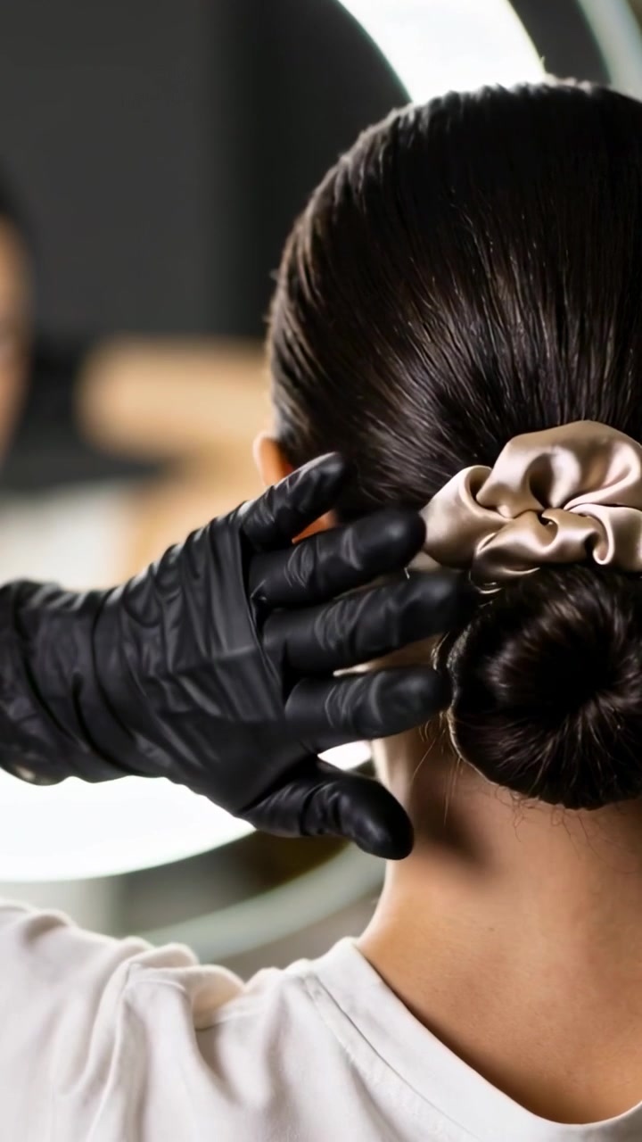 Video verticale: Una mano che entra, stilista guantata che sistema un elastico per capelli su uno chignon in un salone per un controllo.