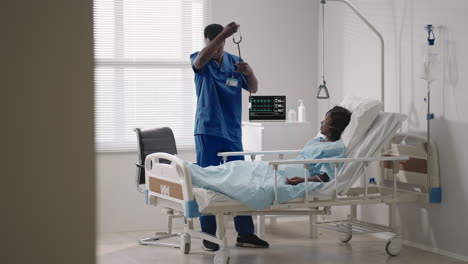 a black male doctor is talking to a black female patient lying on a hospital bed and connected to an acid supply. the attending physician discusses with the patient in the hospital the treatment