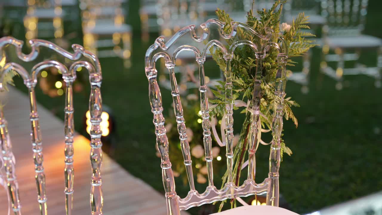Outdoor wedding ceremony setup with decorated aisle floral arrangements and elegant transparent chairs