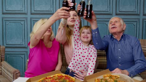 Familia-Multigeneracional-Almorzando,-Comiendo-Pizza,-Riendo,-Levantando-Tostadas-En-Casa