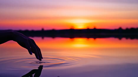 hand gently touching water at sunset