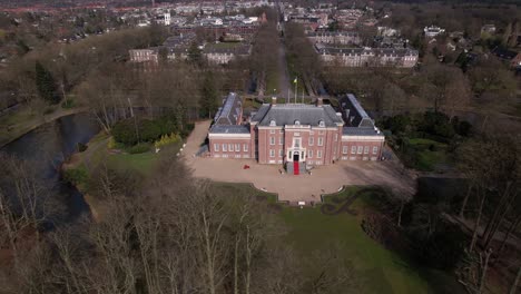 sideways aerial pan around slot zeist castle with the moated manor surrounded by green park and urban landscape in the background