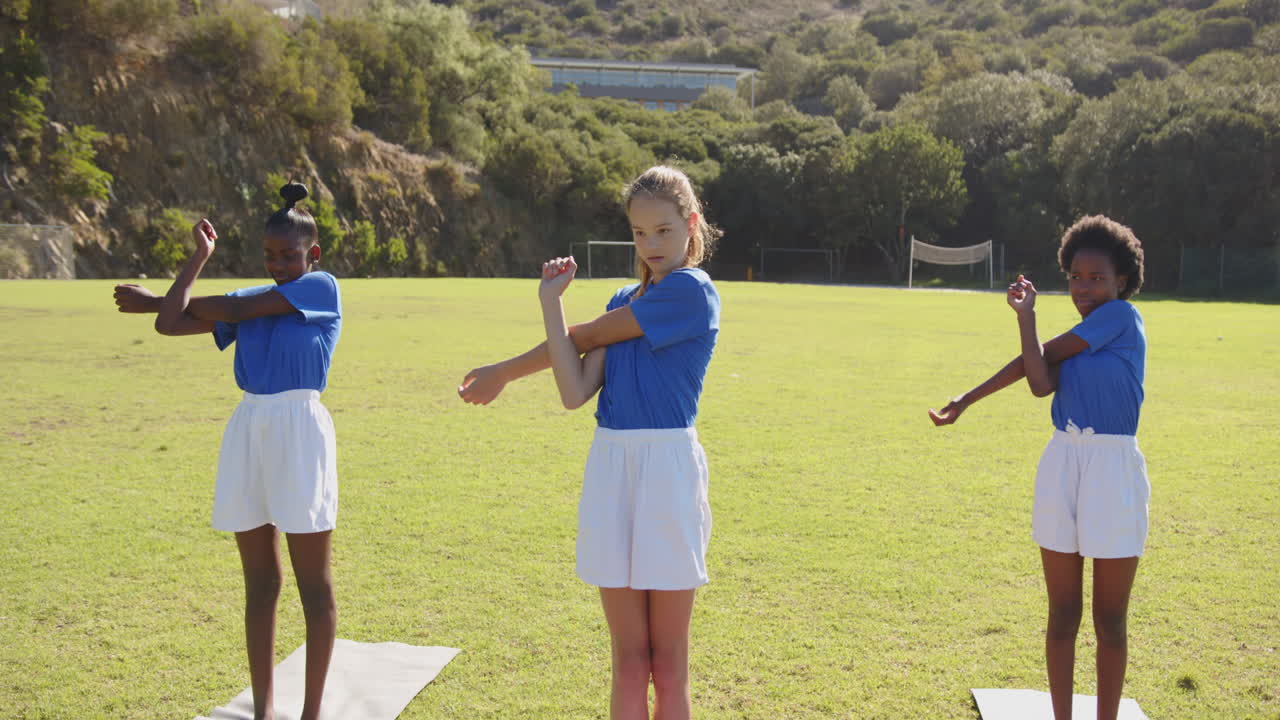 In school, girls stretching on yoga mats during physical education class outside