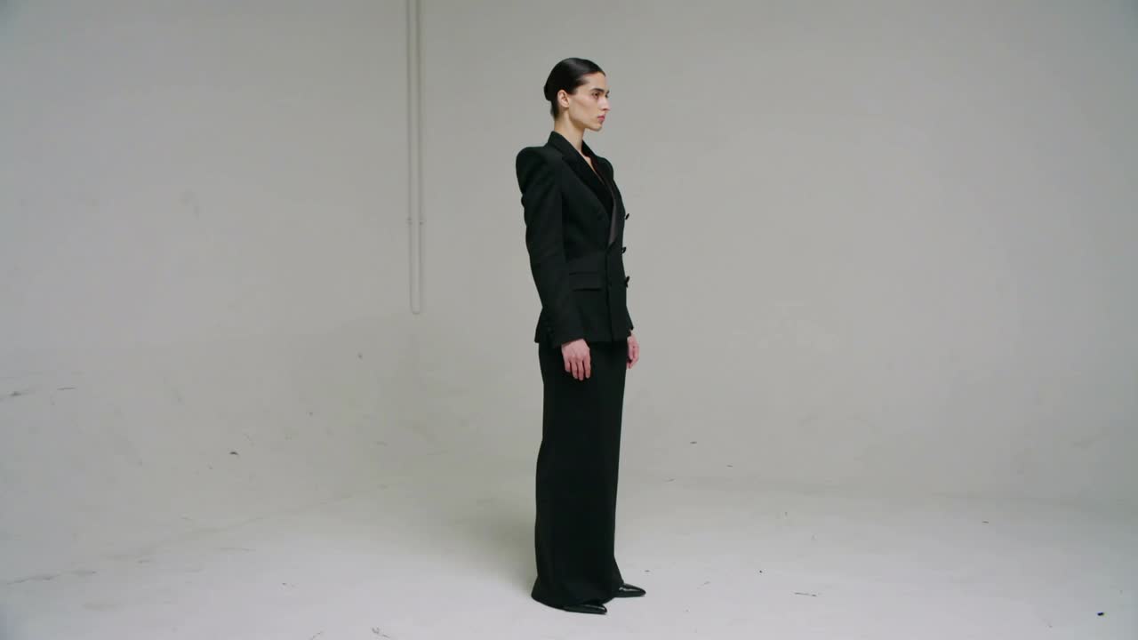 Turning female model from profile into front pose in studio showing black blazer, skirt and conduit
