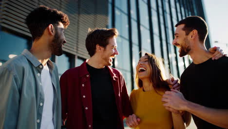 four happy friends laughing together outdoors in front of a modern building