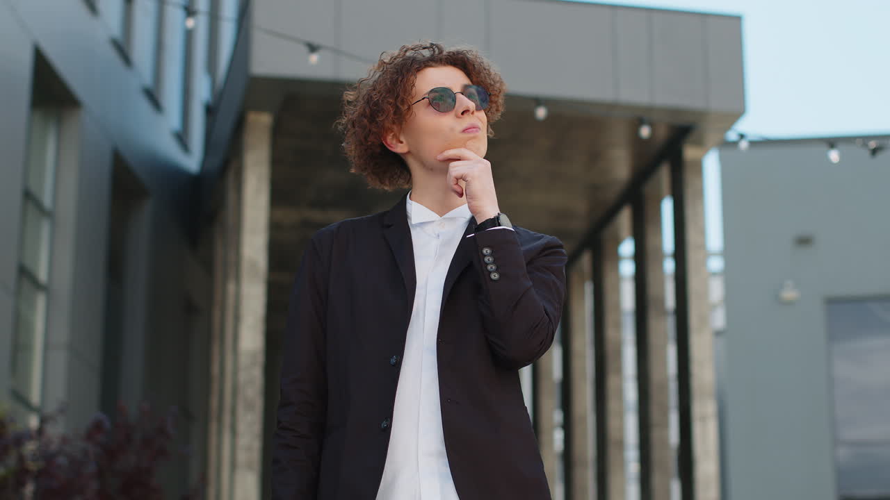 Portrait of puzzled businessman standing outdoors office deep in thoughts thinking creating plan