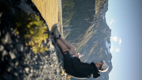 Out-of-focus-hiker-with-water-bottle-sitting-down-at-cliff's-edge-at-sunset