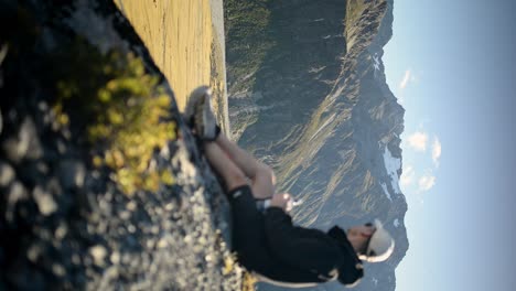 Out of focus hiker with water bottle sitting down at cliff&#039;s edge at sunset