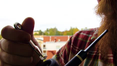 Old-fashioned-vintage-smoking-and-tobacco-pushing-golden-silver-tool-used-on-a-pipe-by-a-ginger-bearded-Caucasian-male-burning-tobacco-releasing-clouds-of-smoke-on-cloudy-day-extreme-close-up