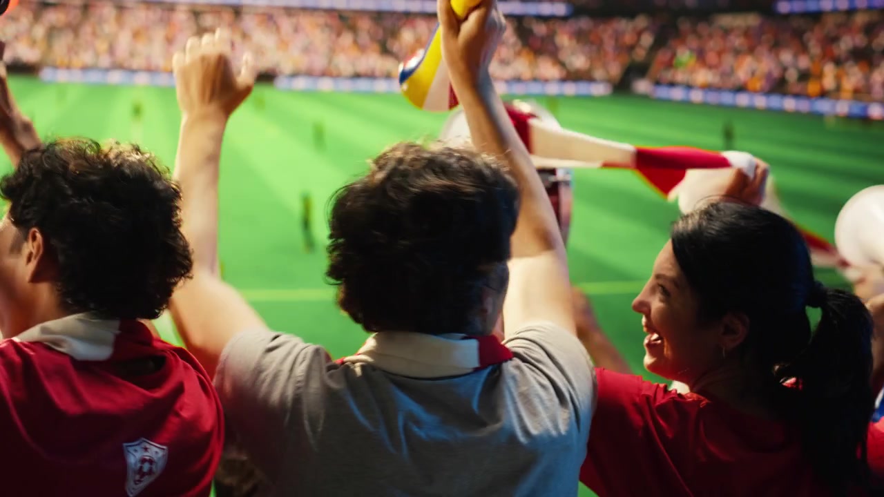Aficionados al fútbol con camisetas rojas reaccionan con emoción a un gol anotado durante el partido