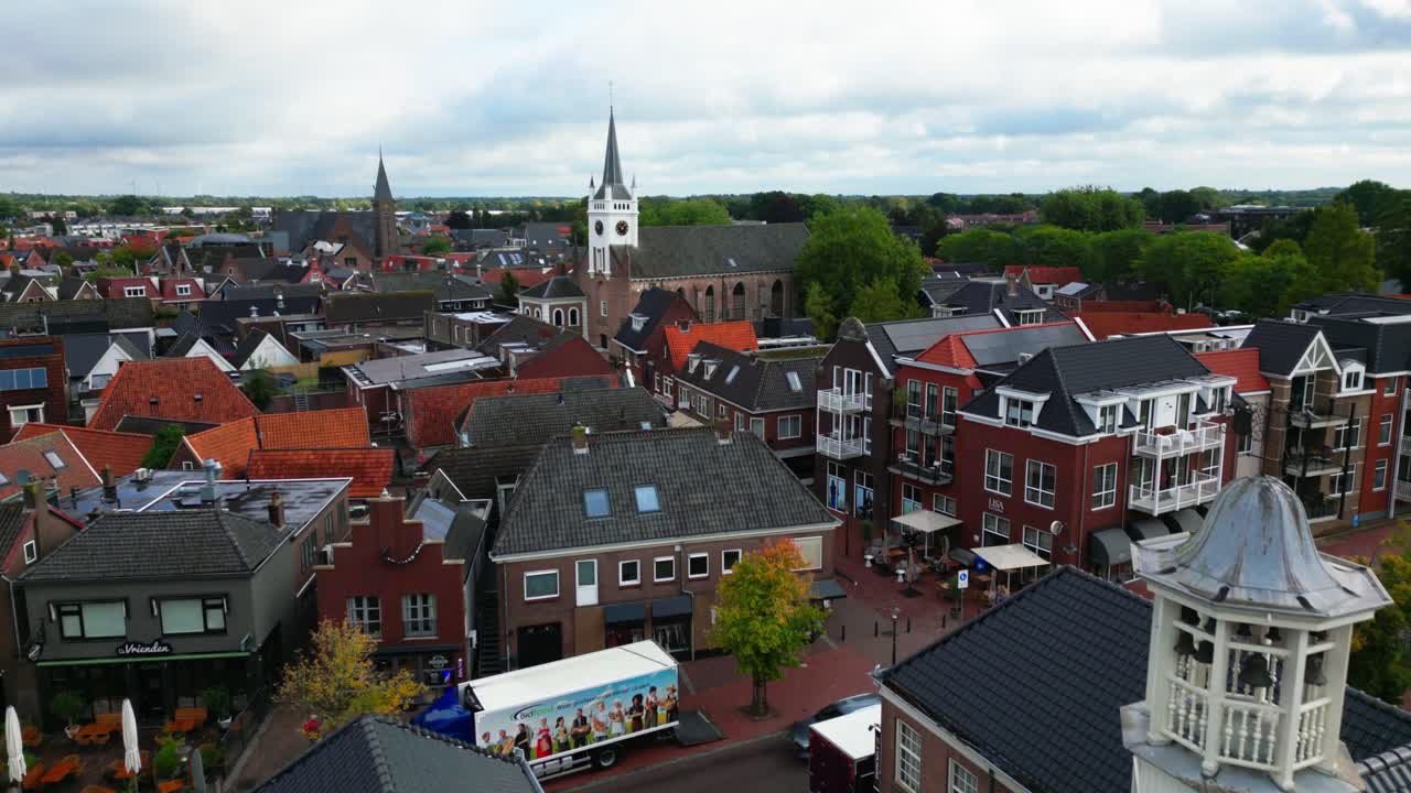 Drone skyline showing Ommen rooftops, tiled houses, and two church towers rising above town center. Captured in Ommen, Overijssel, Netherlands (Ommen, Overijssel, Nederland)