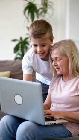 grandson assists his grandmother in using a laptop in the living room.