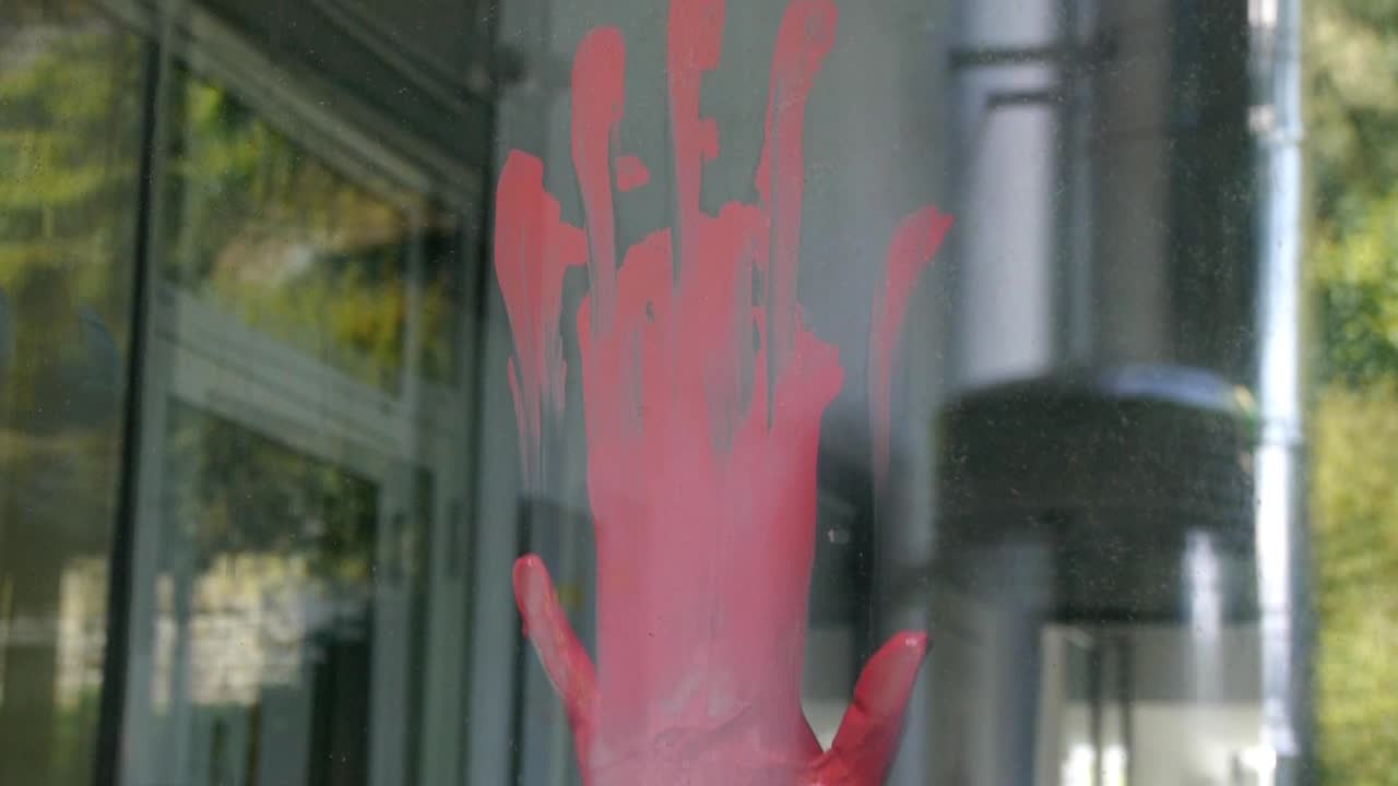 una mano mancha pintura roja en un cristal de ventana, vista desde el exterior, ligero movimiento de cámara