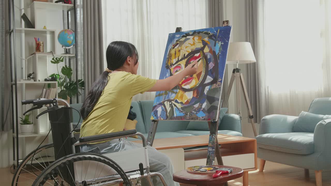 Side View Of An Asian Artist Girl In Wheelchair Holding Paintbrush Mixed Colour Thinking And Painting A Girl On The Canvas