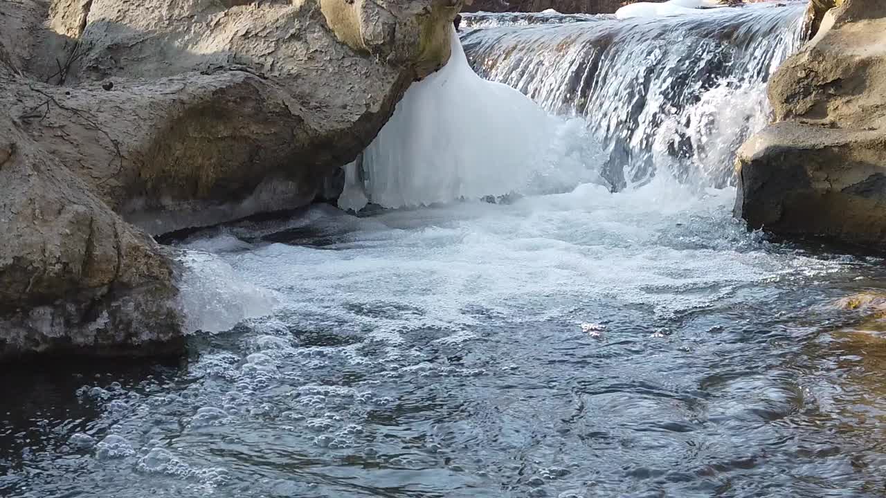 Slow motion dell'acqua tra rocce e ghiaccio, che forma bolle e increspature sulla superficie.