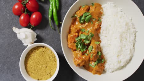 video de un plato con arroz y curry, salsa y tomates en un fondo gris