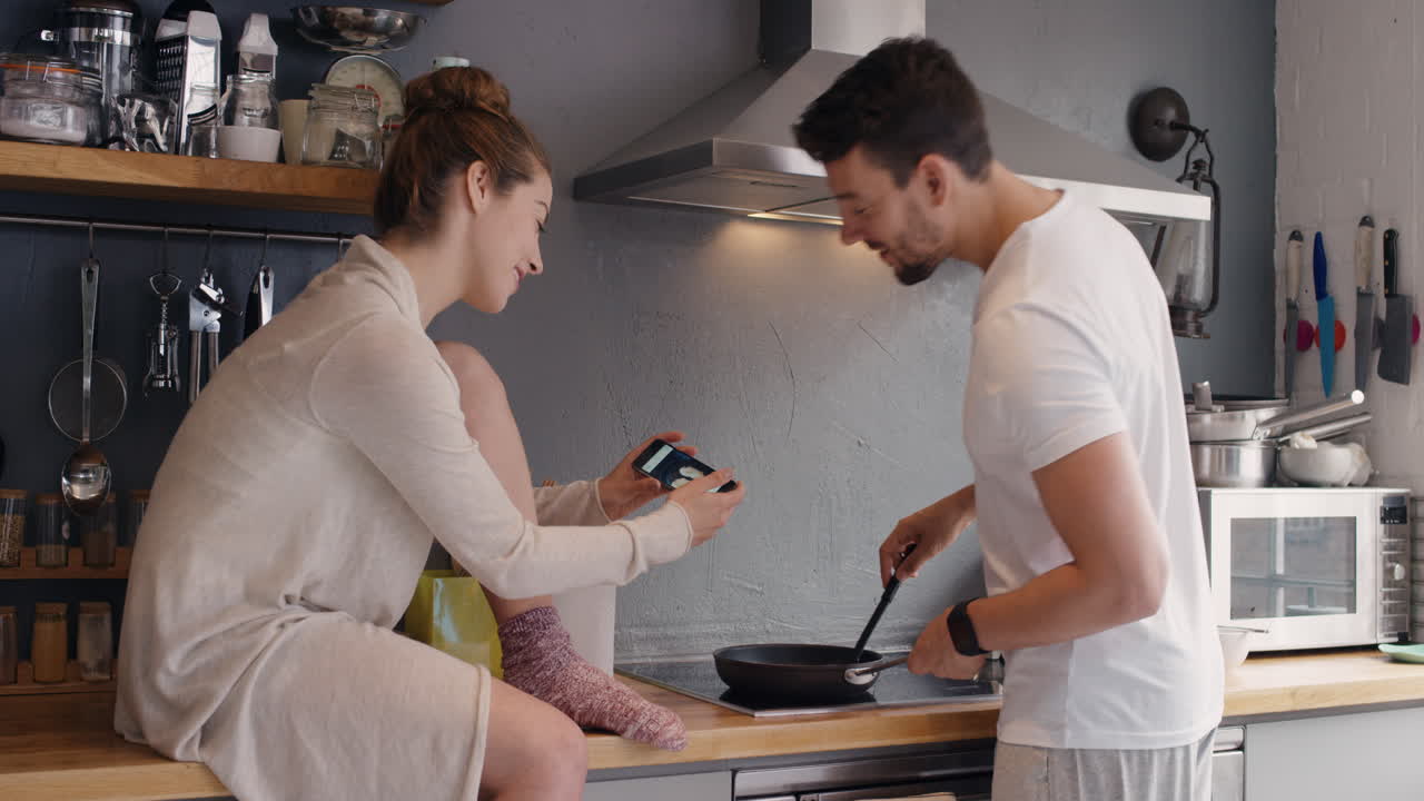 pareja feliz tomando fotos usando el teléfono inteligente del desayuno freyendo huevos para los medios sociales estilo de vida en casa en la cocina