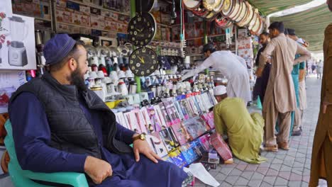 vibrant islamabad market scene captures people enthusiastically haggling and shopping while a shopkeeper looks up with a warm smile to greet the camera.