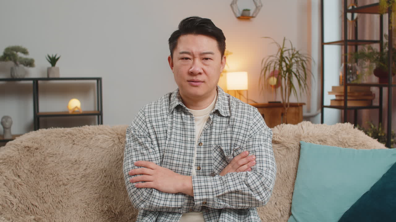 Upset man showing thumbs down sign gesture expressing discontent sitting on sofa couch at home