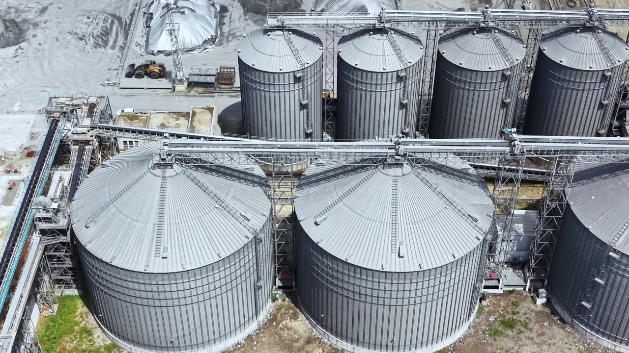 Große Lagersilos auf einem Industriegelände in einem geschäftigen Hafenbereich zeigen das Ausmaß der tagsüber stattfindenden landwirtschaftlichen Verarbeitung.