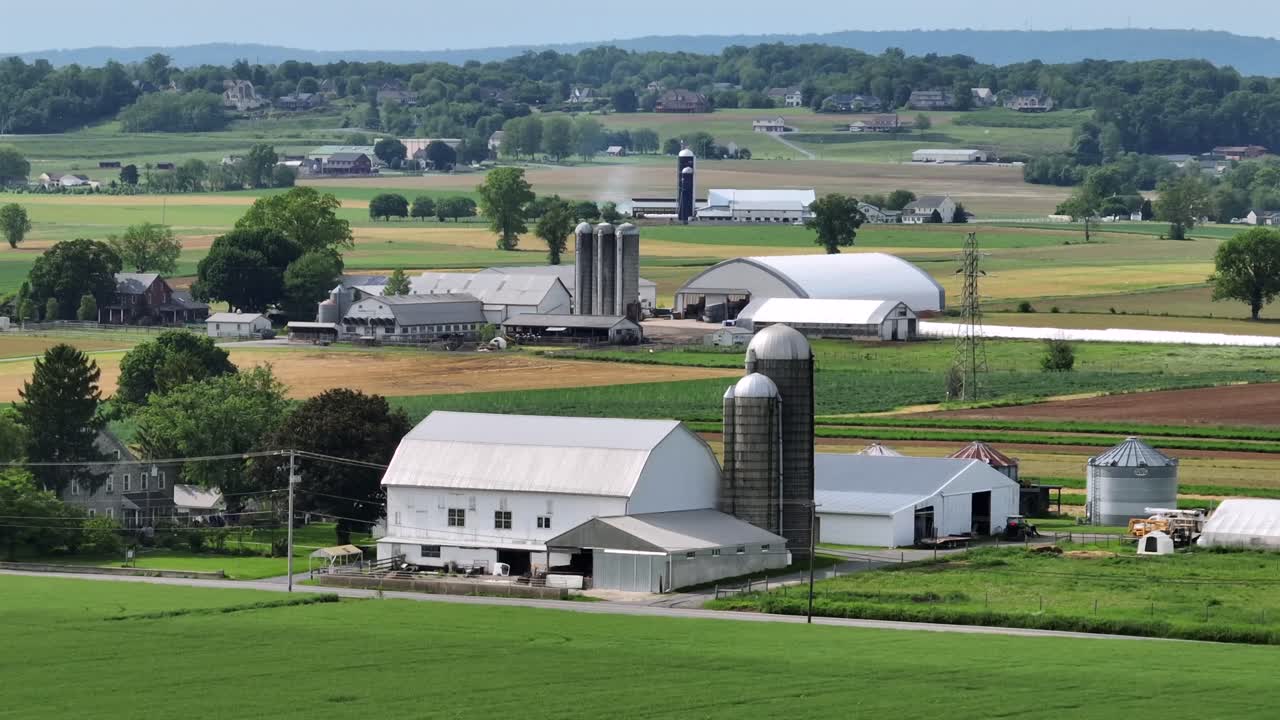 Cars on rural street in front of american farmers house. Silo storage, barn and greenhouse during sunny day in spring. Aerial zoom wide shot. Agricultural theme.