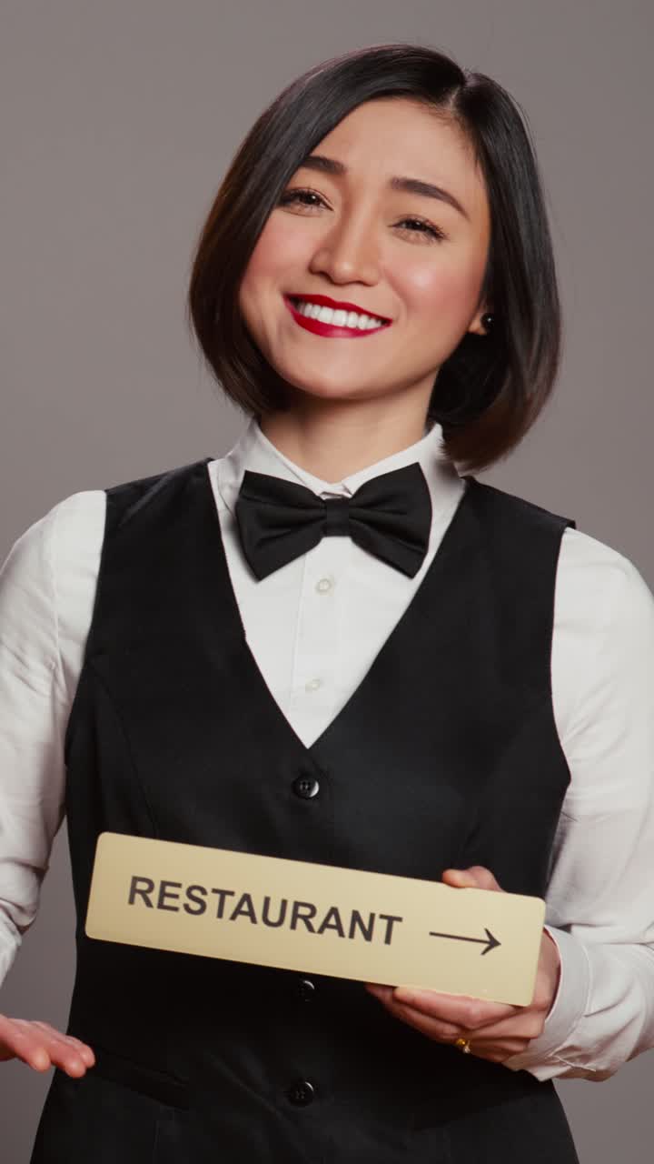 Video verticale: concierge asiatico di un hotel che regge un cartello del ristorante per indicare la direzione