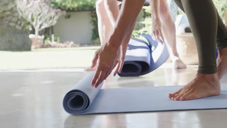 Close-up-of-diverse-seniors-preparing-exercise-mats-for-pilates-class,-unaltered,-in-slow-motion